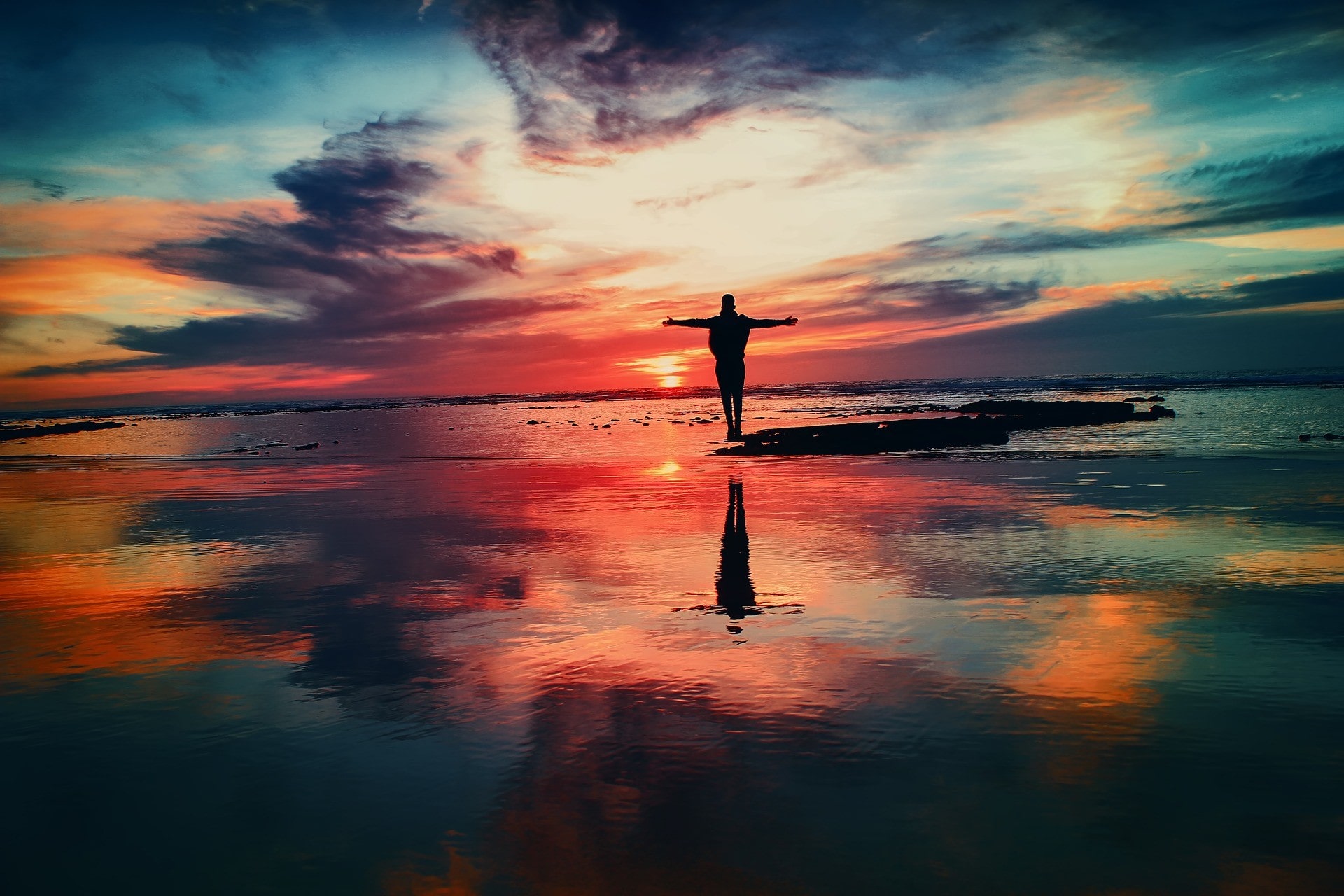 Silhouette of a person standing on the beach with arms outstretched taking in the glorious sunrise.